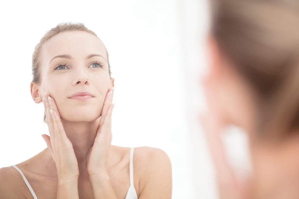 Young woman looking in mirror, applying moisturiser to face