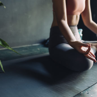 Close up of a woman in sportswear sitting on a yoga mat and meditating.