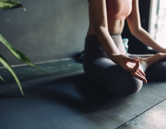 Close up of a woman in sportswear sitting on a yoga mat and meditating.