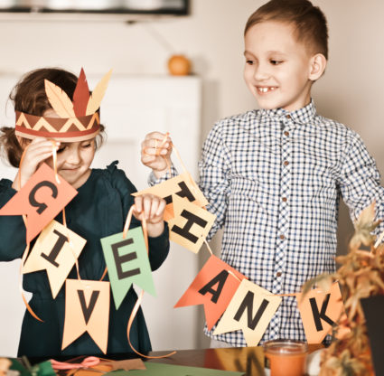 Kid holding paper garland with text Give thanks. Children decorating living room for celebrating Thanksgiving day.