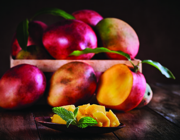 Tropical fruits. Group of ripe mangos on a crate in rustic table with mango slice.