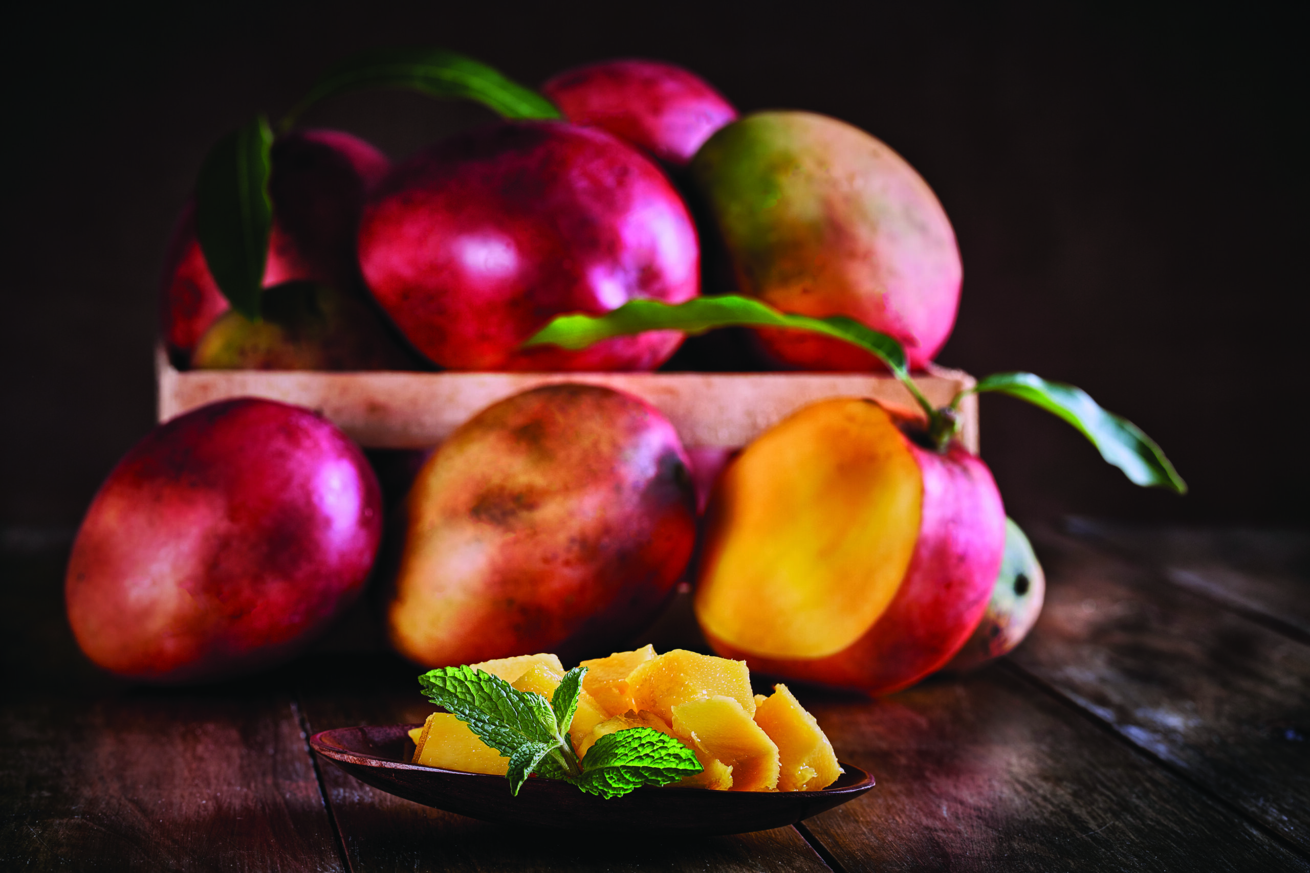 Tropical fruits. Group of ripe mangos on a crate in rustic table with mango slice.